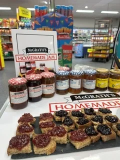 A tasting table of McGrath’s jam on brown bread squares, jars lined up behind the board